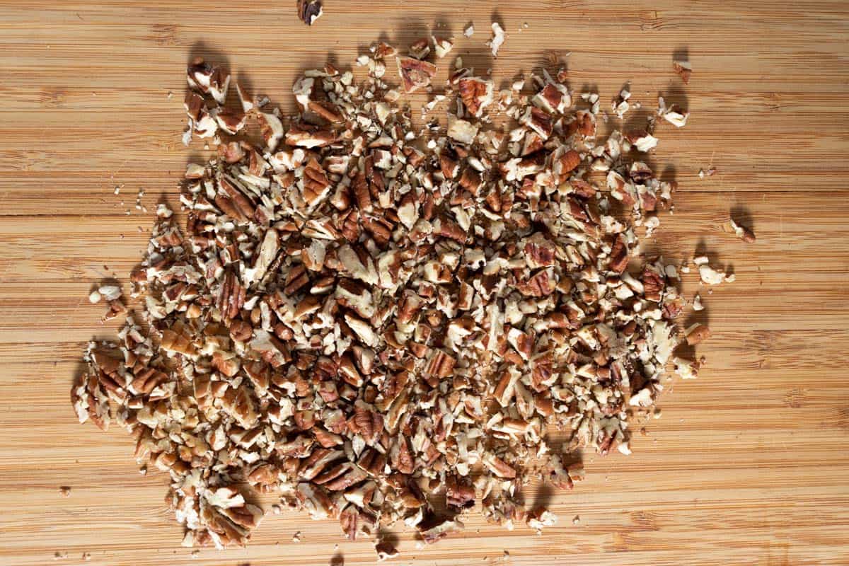 Chopped toasted pecans on a wooden cutting board.