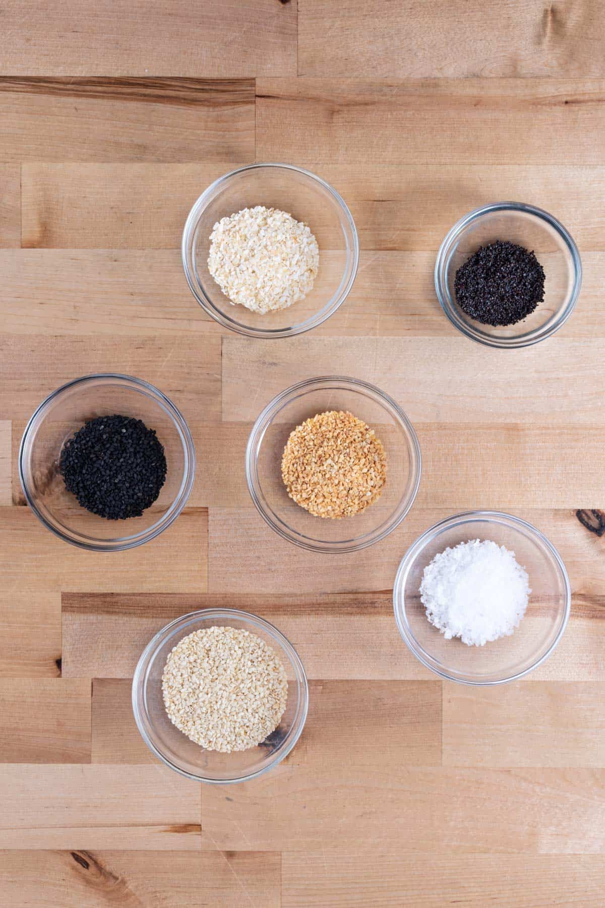 Bowls of sesame seeds, poppy seeds, minced garlic, minced onion, and sea salt flakes.