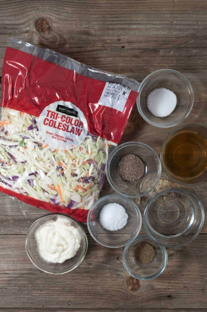 A bag of tri-color coleslaw mix and the ingredients for dressing on a wooden table.