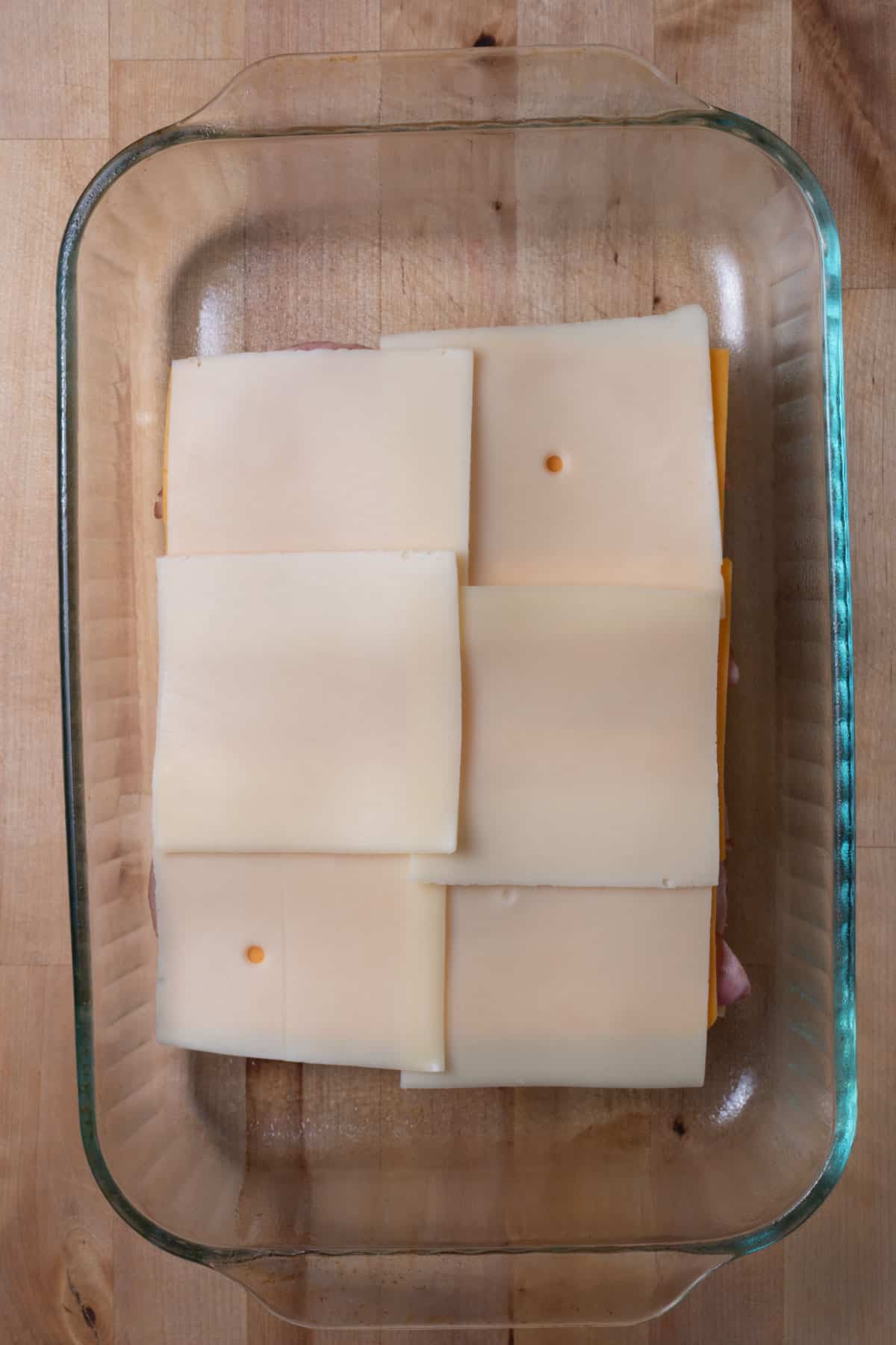 Cheese slices on top of buns in a glass baking dish.