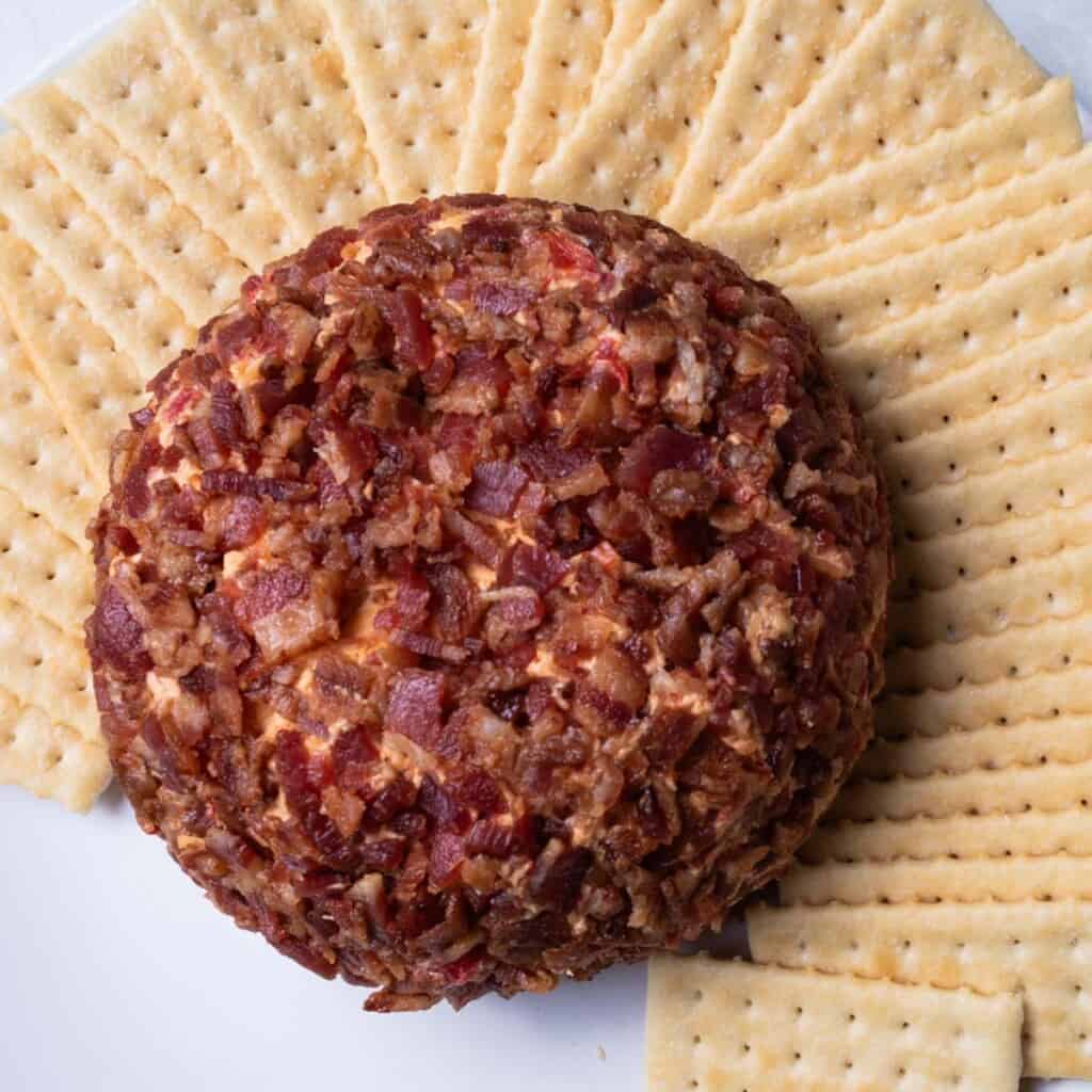 Pimento cheese ball on a white plate, surrounded by club crackers.