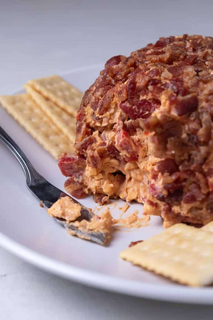 A bacon coated pimento cheese ball served on a platter with club crackers.