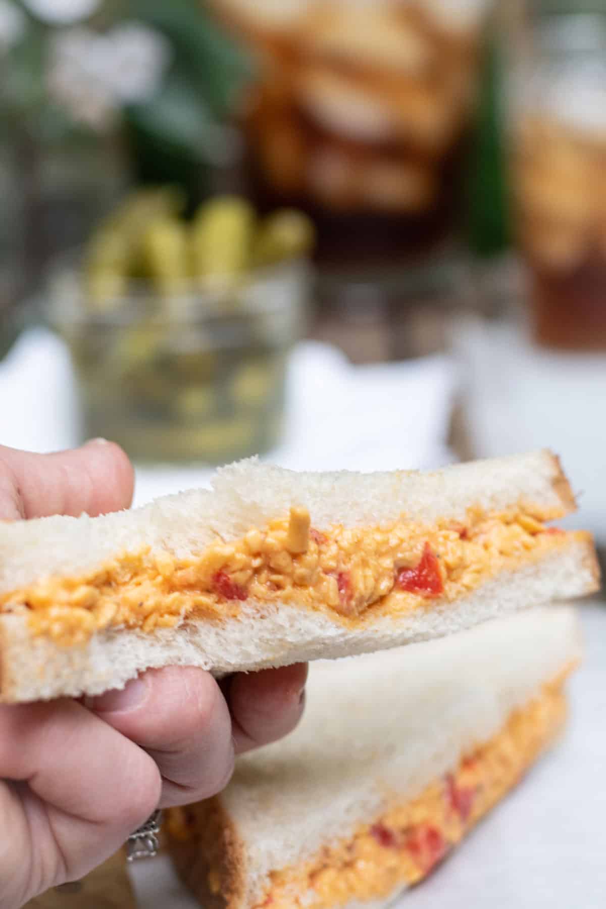Up close of pimento cheese sandwich with pickles and sweet tea in the background.