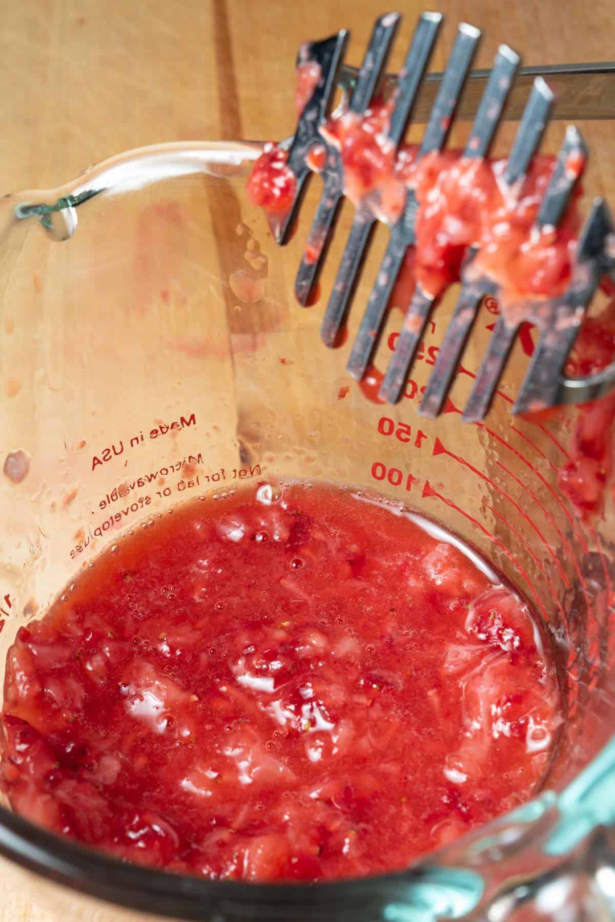 Crushed strawberries in a glass measuring cup.