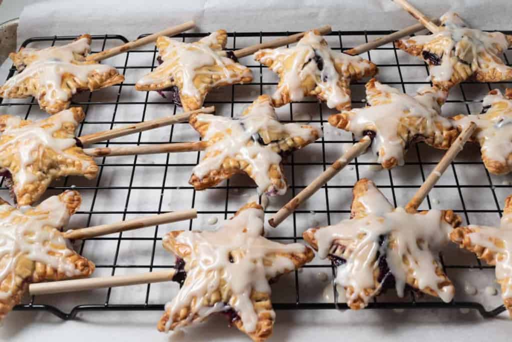 A cooling rack filled with individual star shaped blueberry pie pops.