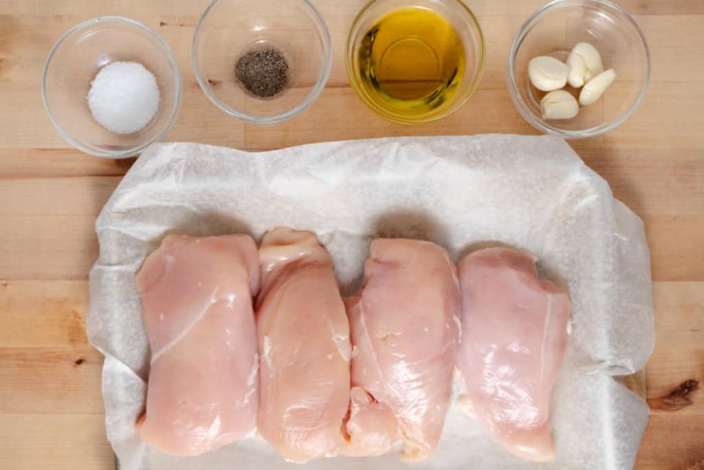 Raw boneless skinless chicken breasts with ingredients for marinade.