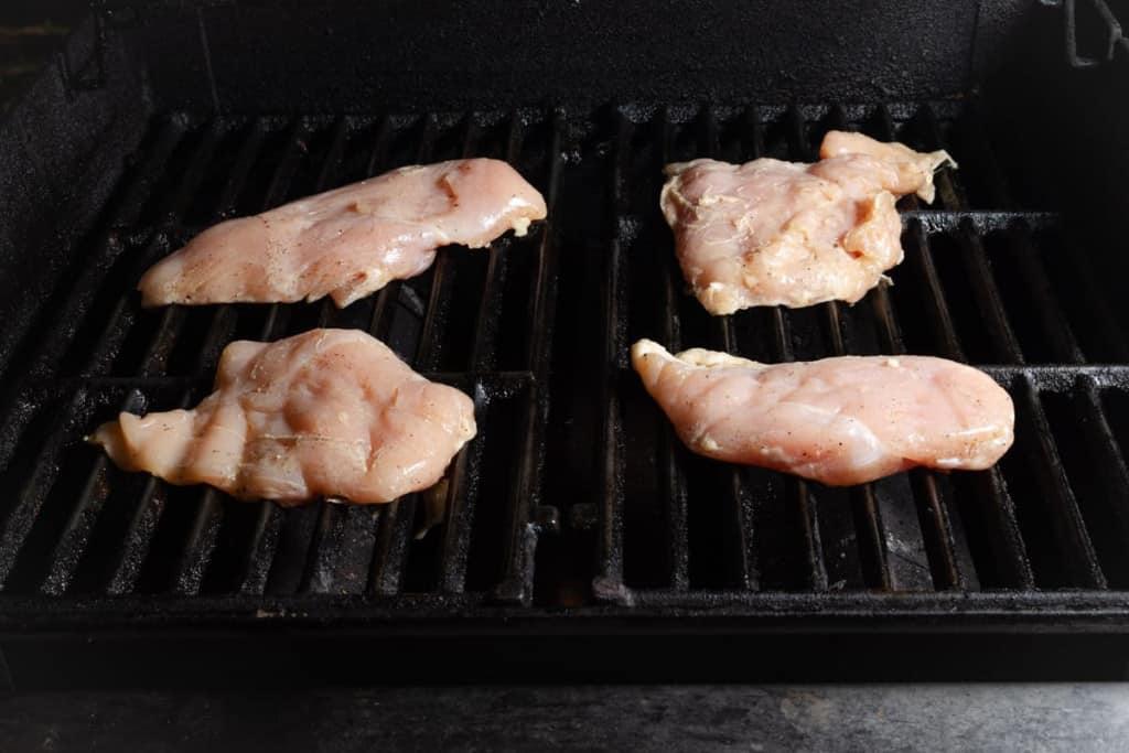 Raw boneless skinless chicken breasts on a grill.