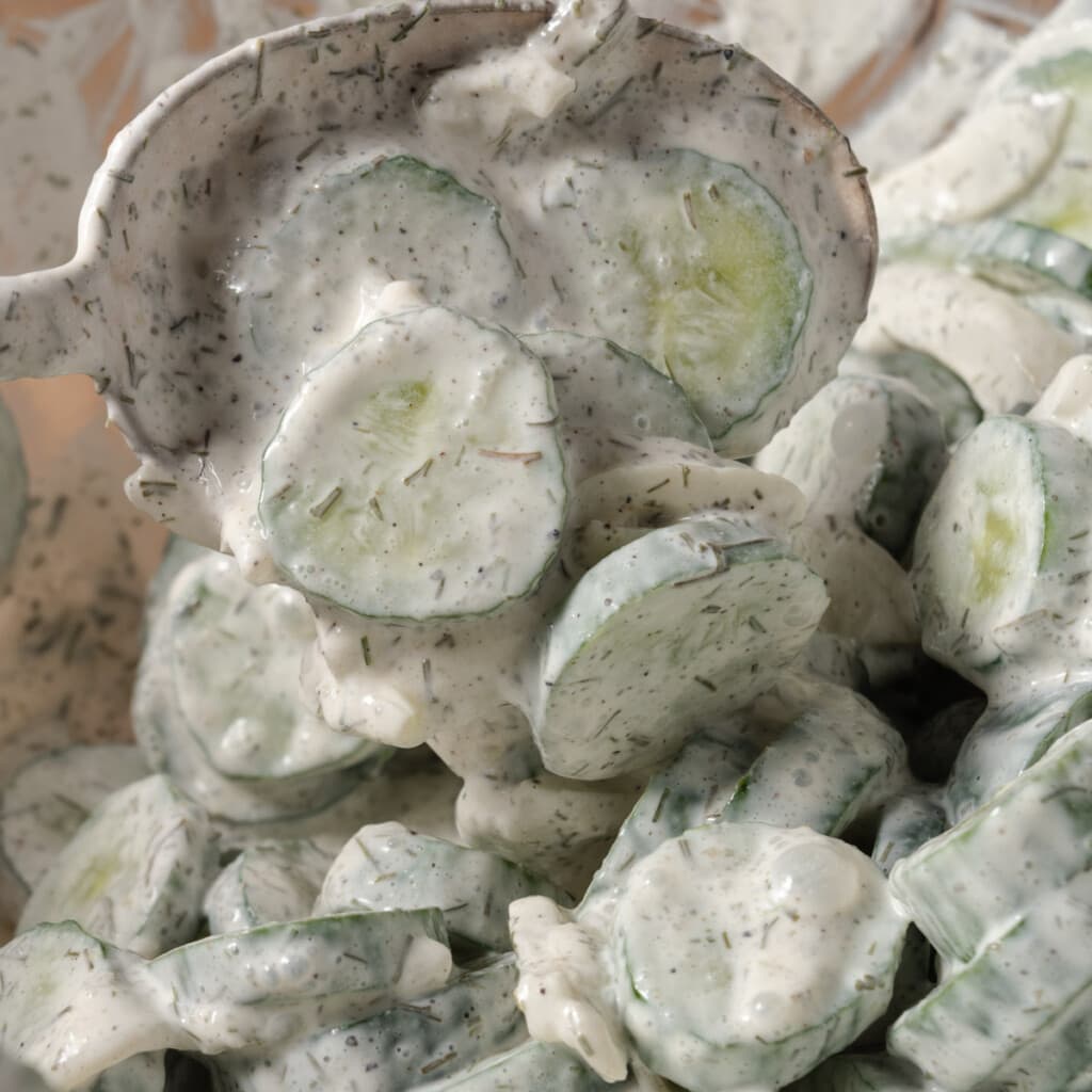 A spoon stirring a bowl of creamy cucumber salad.