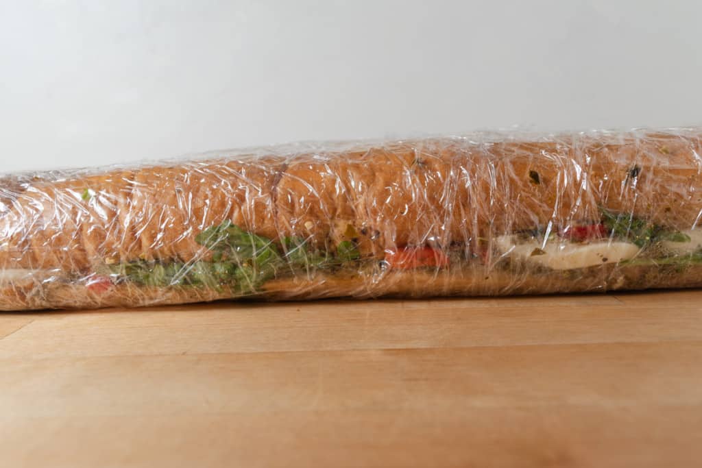 Sandwich made from a loaf of French bread, wrapped in plastic wrap.