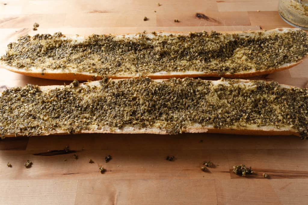 A loaf of French bread, cut in half and covered with pesto.