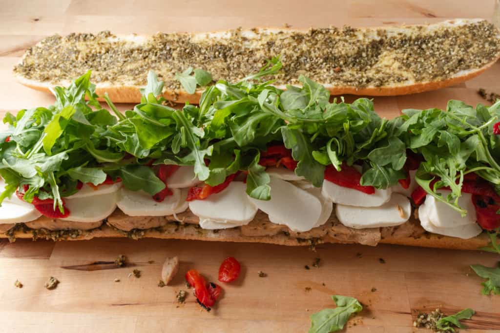 Freshly made party sandwich with chicken, pesto, mozzarella, roasted red peppers, and arugula.