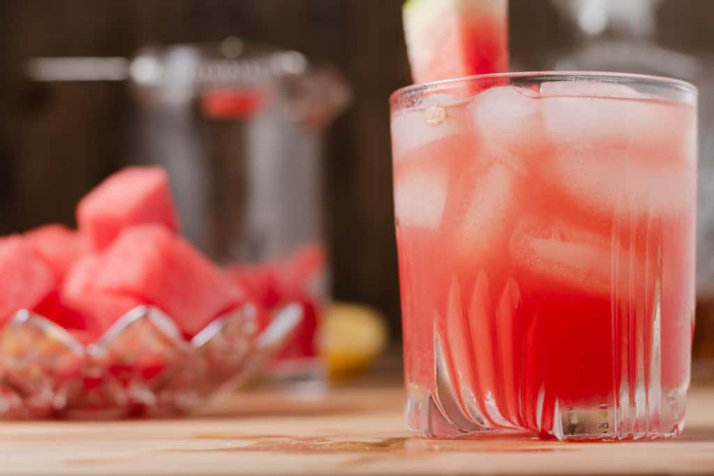 A watermelon sour with a dish of watermelon and a decanter of bourbon in the background.