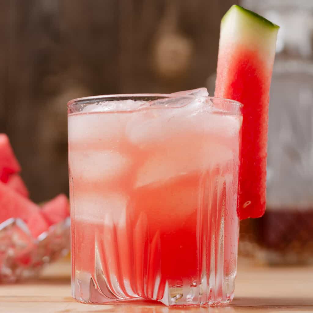 A watermelon whiskey sour cocktail with bourbon and a dish of watermelon in the background.