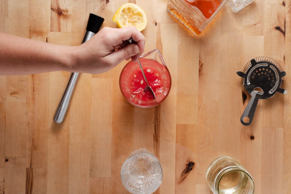 Stirring a cocktail glass of watermelon sour.