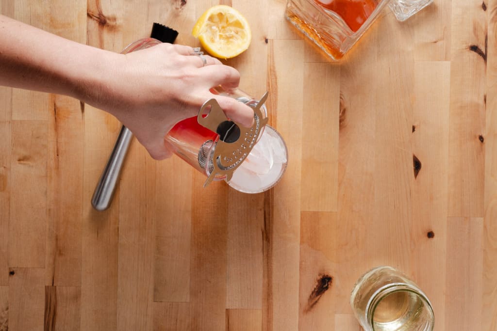 Straining a watermelon cocktail into a glass of ice.