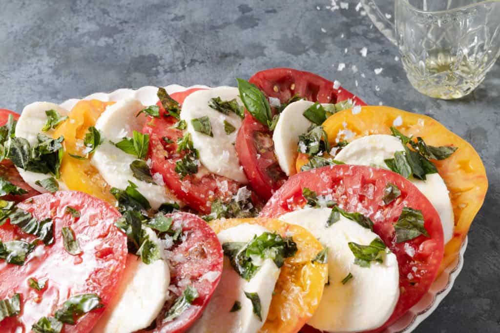 Sprinkling salt flakes on caprese made from red, yellow, and Cherokee purple heirloom tomatoes.