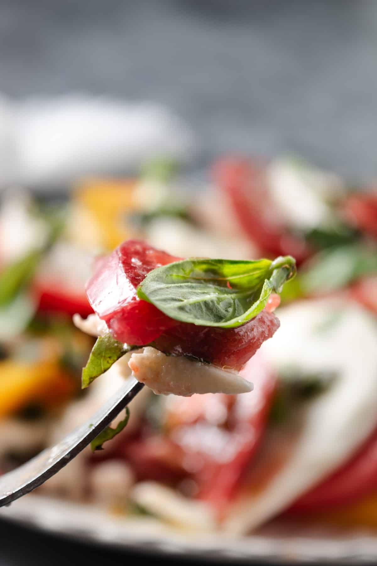 A perfect bite of heirloom caprese with tomato, mozzarella, and basil.