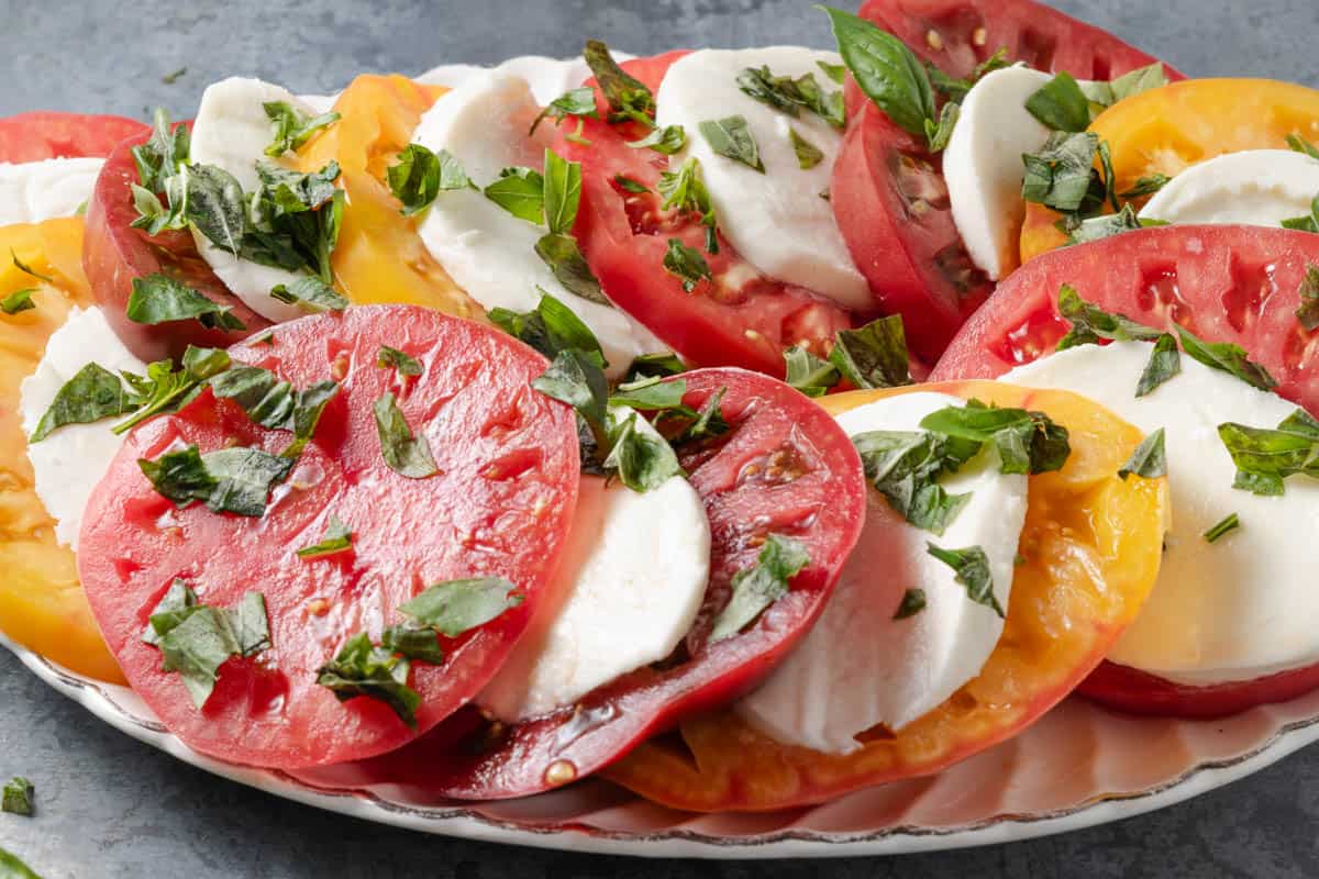 Perfectly arranged caprese made from red, yellow, and Cherokee purple heirloom tomatoes with mozzarella and basil.