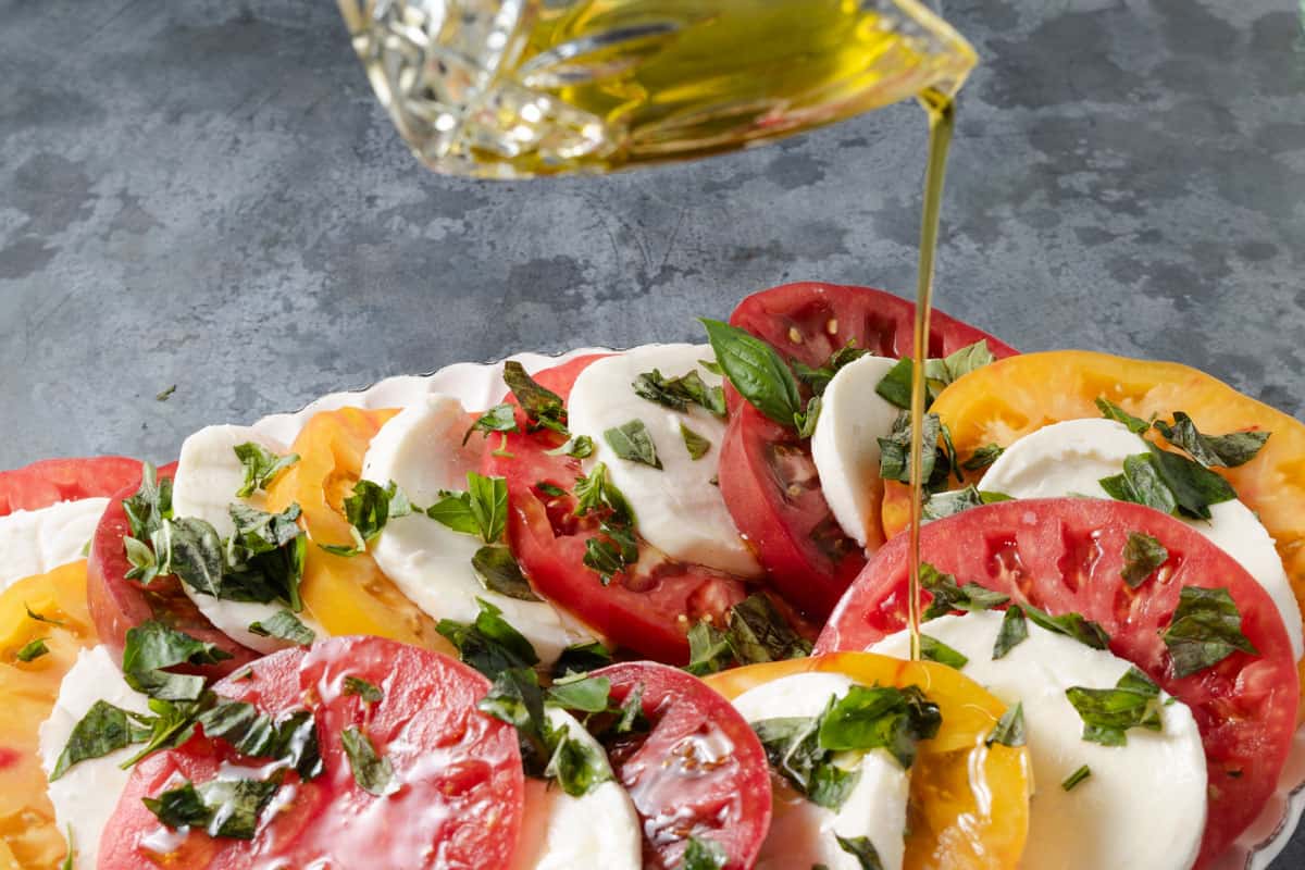 Pouring extra virgin olive oil on caprese made from red, yellow, and Cherokee purple heirloom tomatoes.