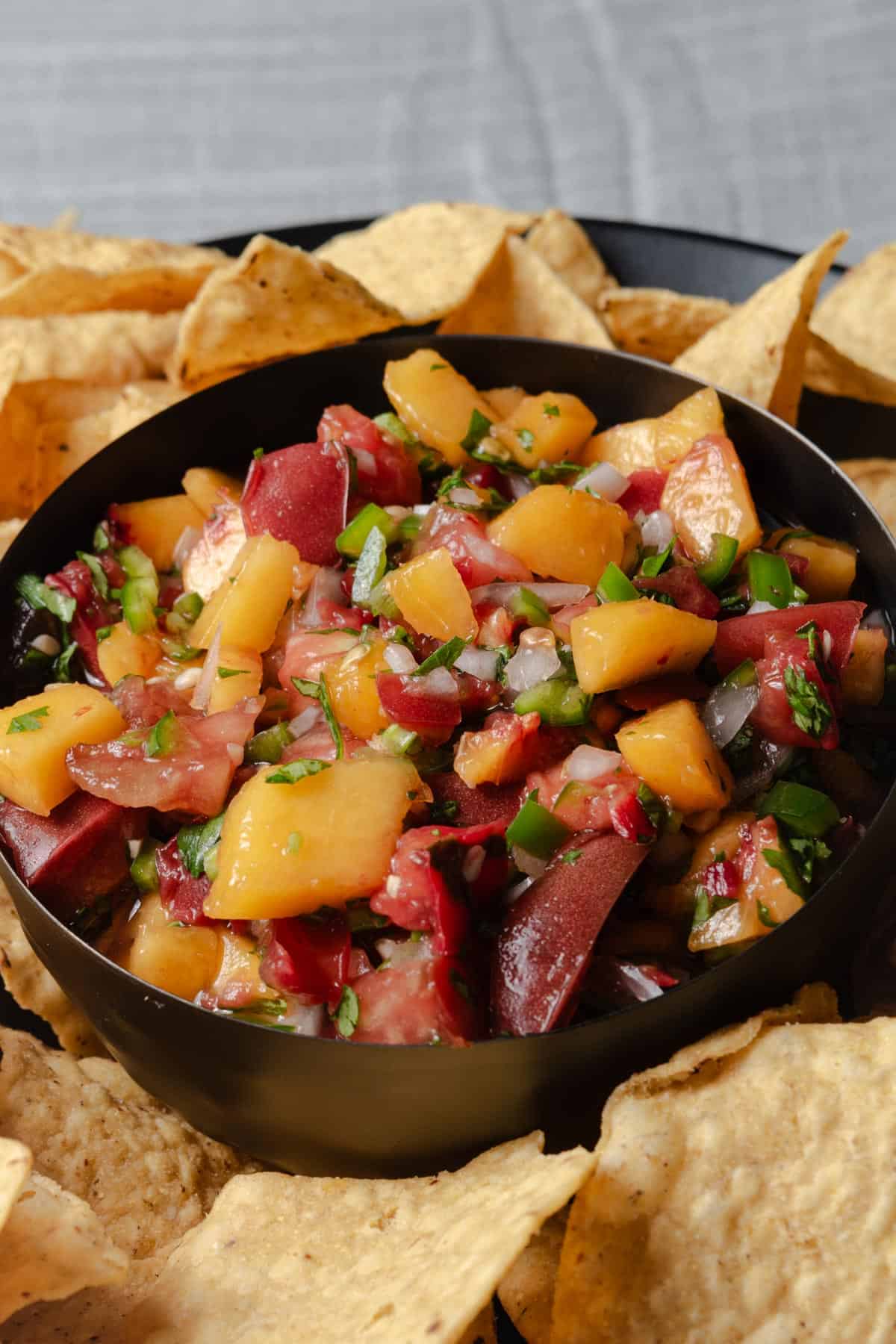Spicy peach salsa in a bowl with a plate of tortilla chips.