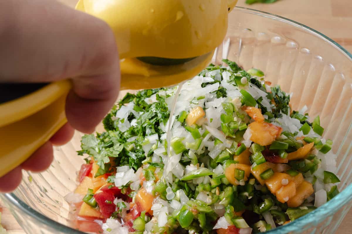 Squeezing lime juice into a bowl of peach pico de gallo.