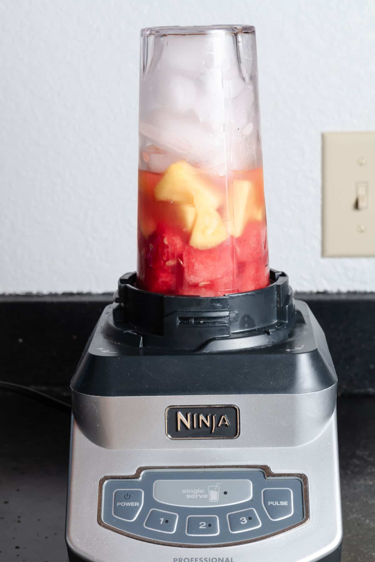 Watermelon, pineapple, coconut water, and ice in a blender.