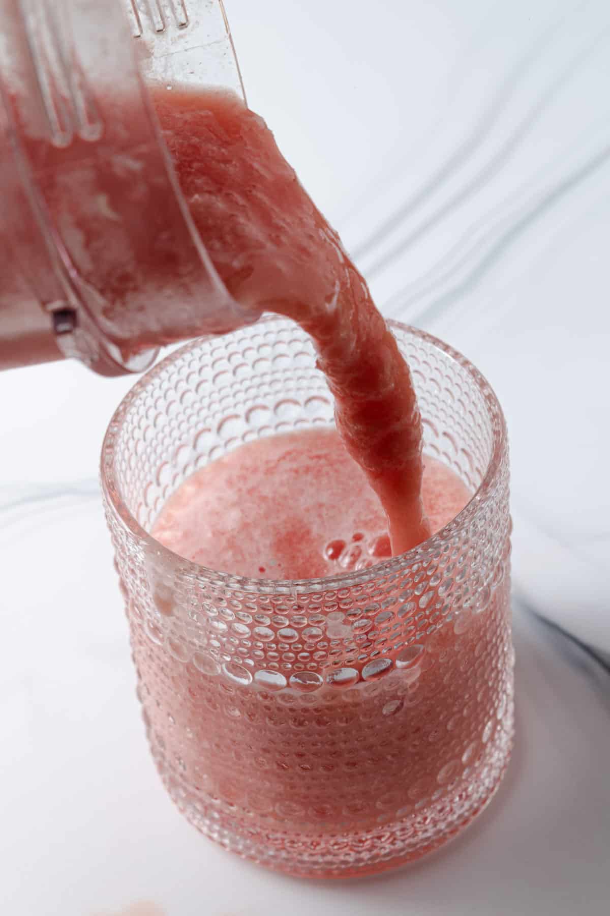 Pouring a blended watermelon pineapple drink from a blender into a glass.