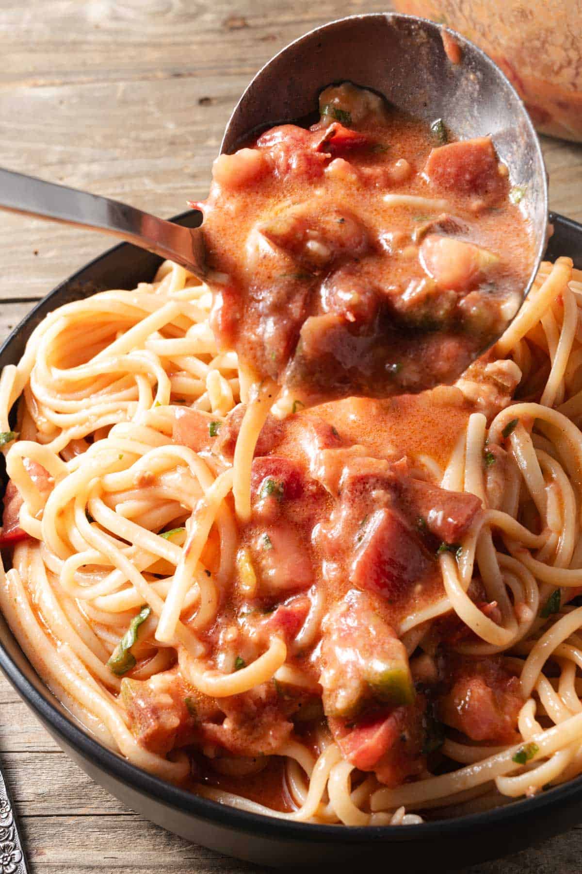 Ladling fresh tomato and brie pasta sauce over a bowl of linguine noodles.
