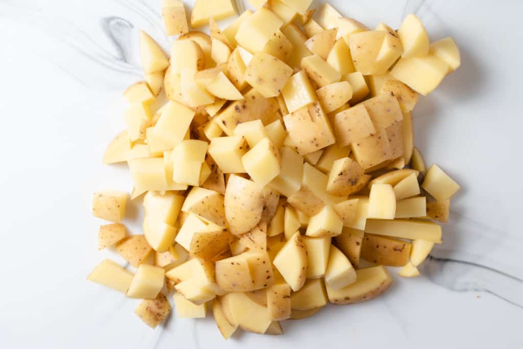 A pile of diced potatoes on a white cutting board.