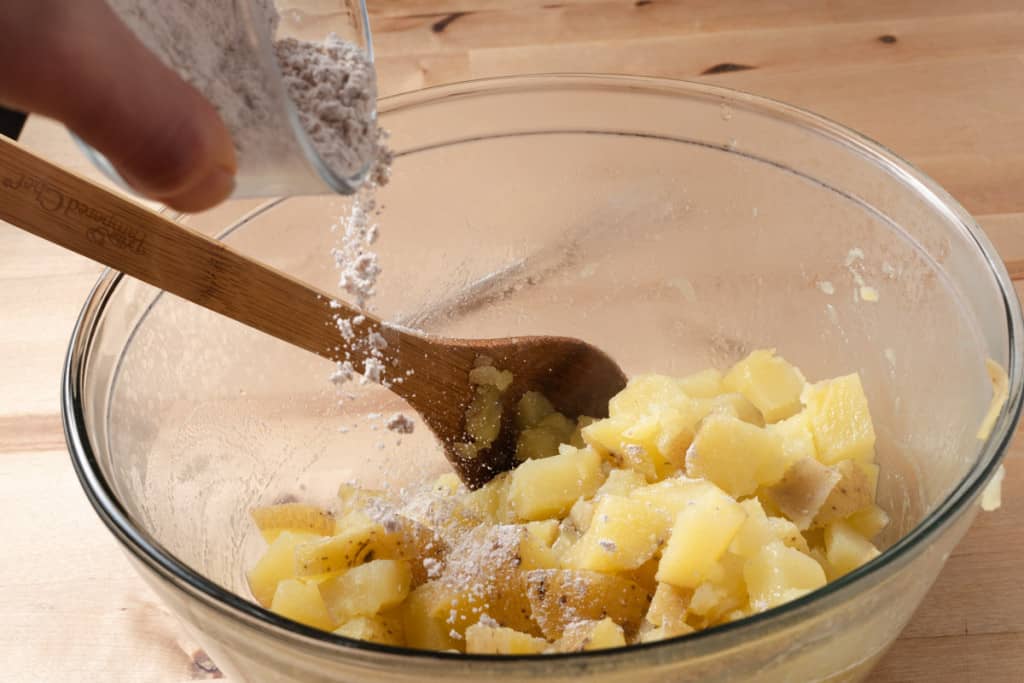 Sprinkling Mexican seasoning over a bowl of partially cooked potatoes.