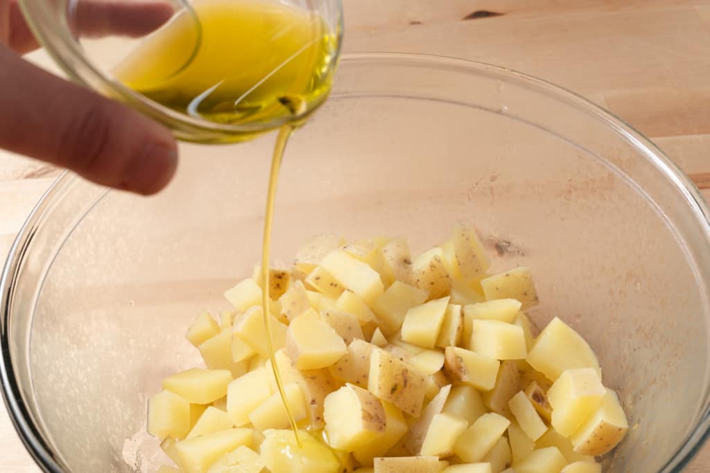 Drizzling olive oil over partially cooked potato pieces in a bowl.