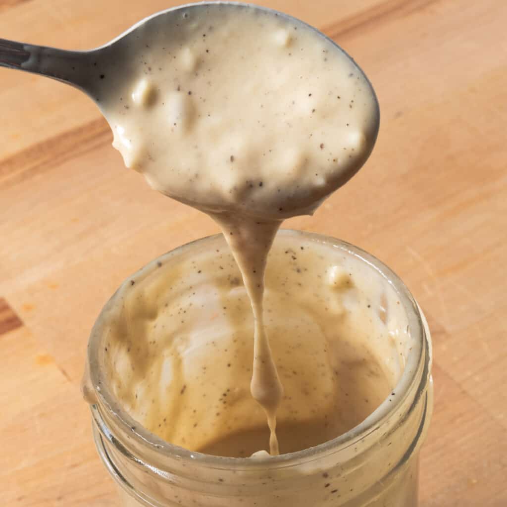 Honey tahini dressing dripping from a spoon, into a jar.