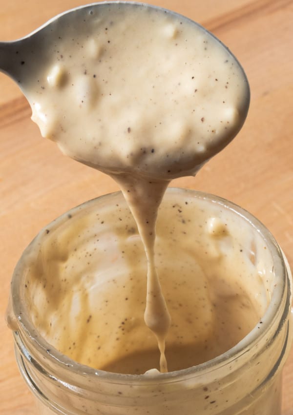 Honey tahini dressing dripping from a spoon, into a jar.