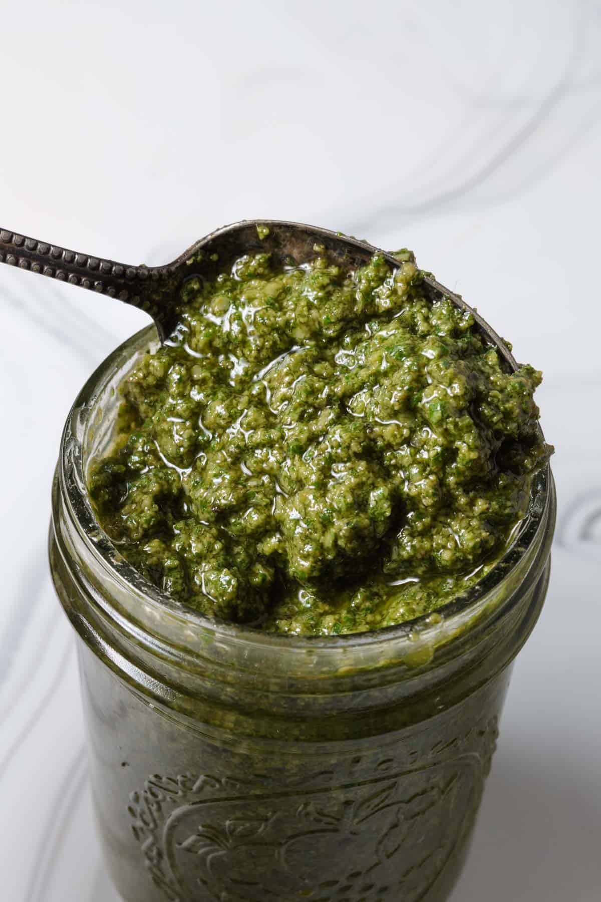 Scooping up pesto from a jar with a spoon.