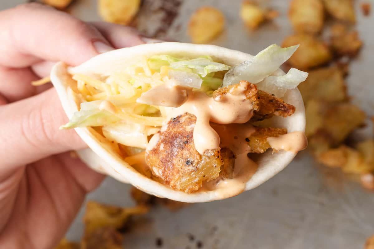 Close up of a hand holding a spicy potato soft taco.