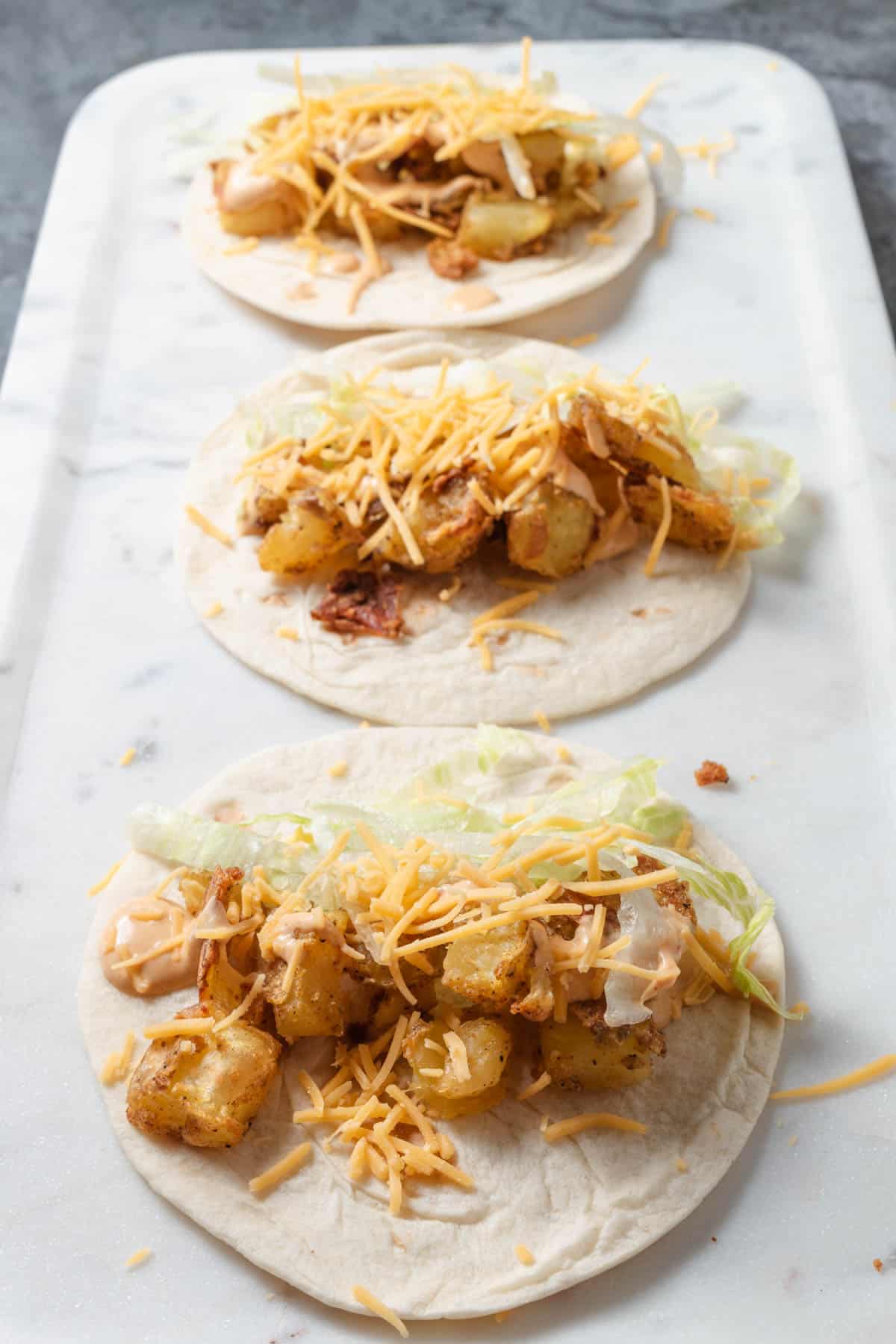 Three spicy potato tacos laid out on flour street taco tortillas.