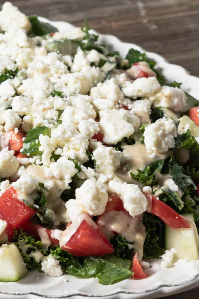 Close up kale salad with cucumber tomato, feta, and tahini dressing.