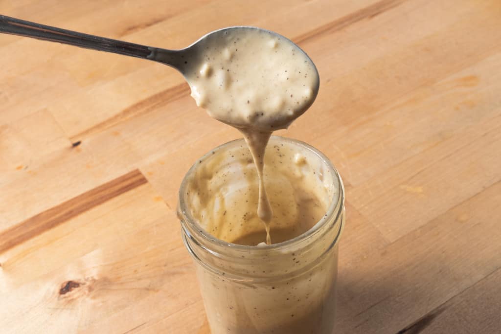 Pouring creamy tahini dressing into a mason jar.