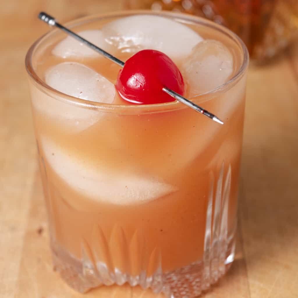 Apple butter bourbon cocktail on the rocks with a cherry.