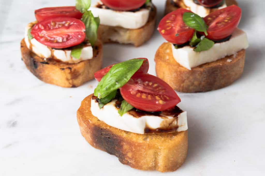 A platter of caprese crostini with balsamic, tomato, mozzarella, and basil.