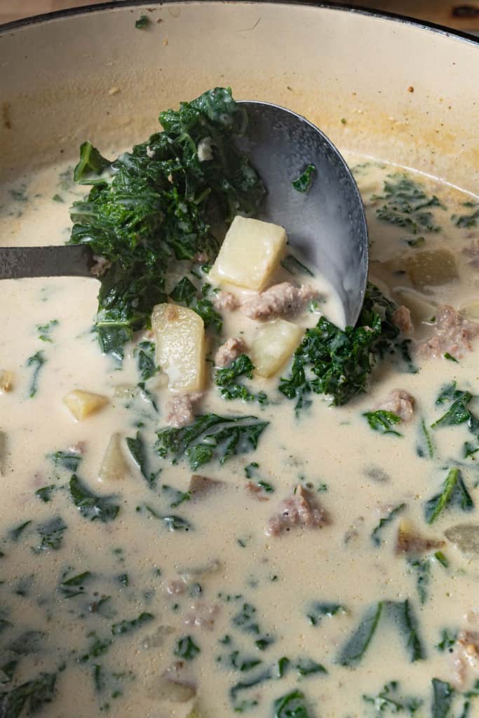 Ladling creamy Italian sausage and kale soup from a pot.