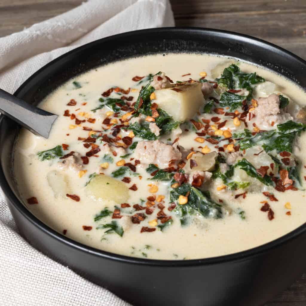 A bowl of creamy Italian sausage soup with potatoes, kale, and red pepper flakes.