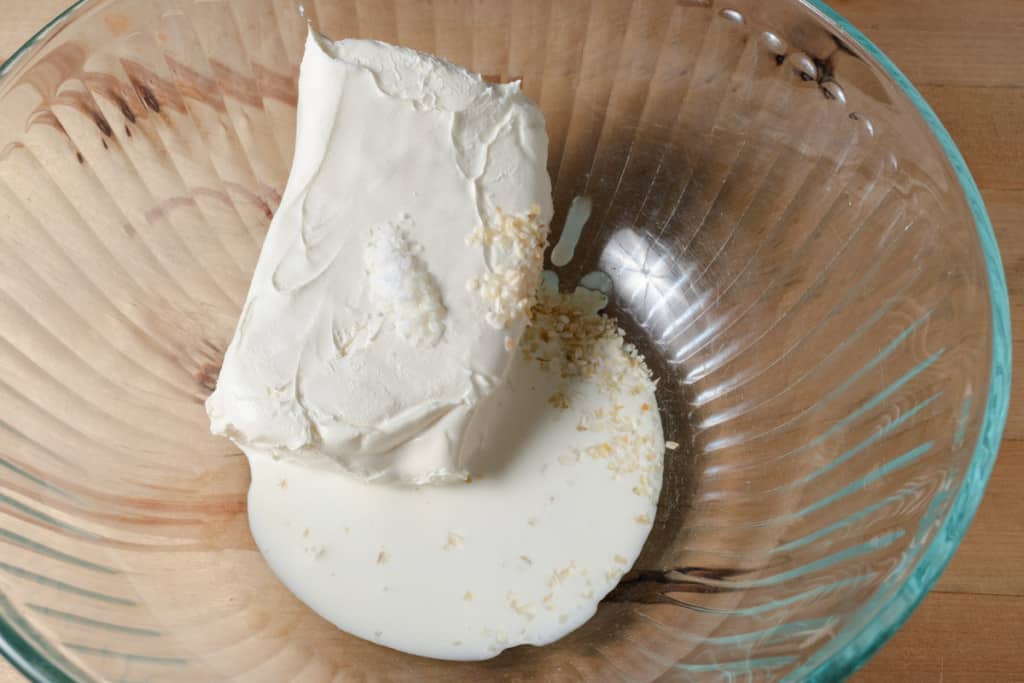 A block of cream cheese with cream, dried onion, and salt in a mixing bowl.