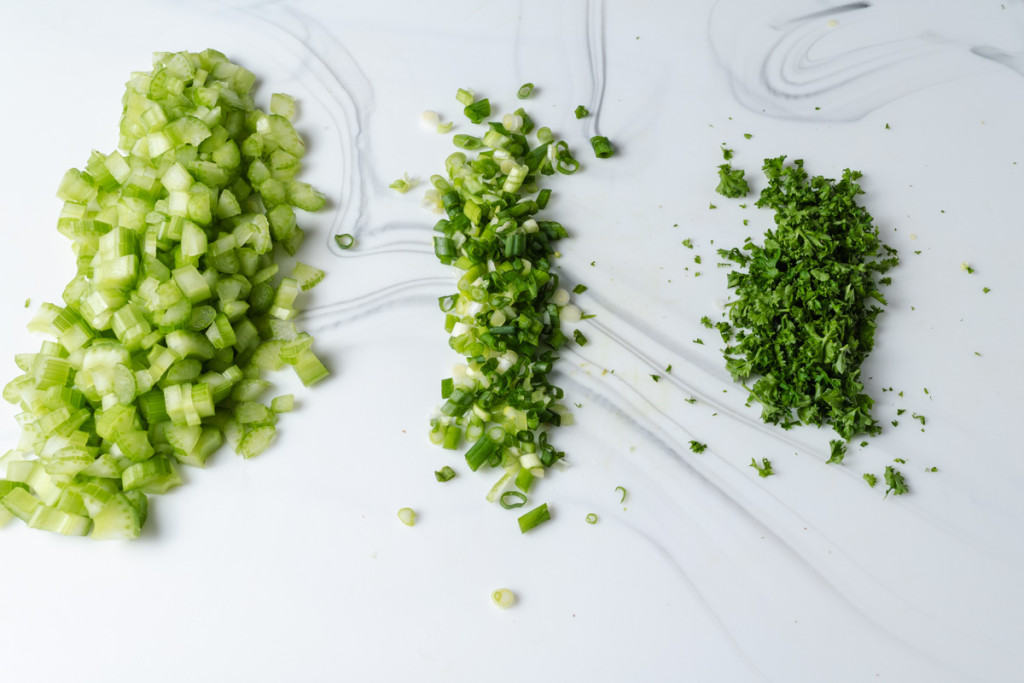 Chopped herbs and celery on a cutting board.