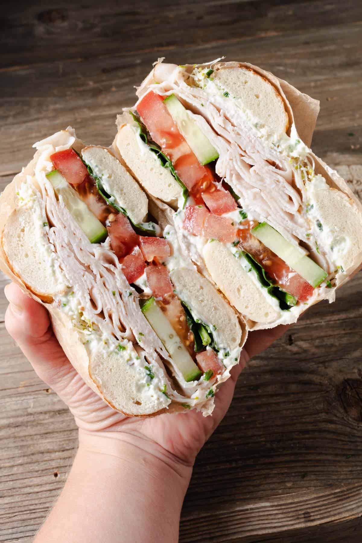 Cross section of a bagel sandwich with turkey, cream cheese, and vegetables.