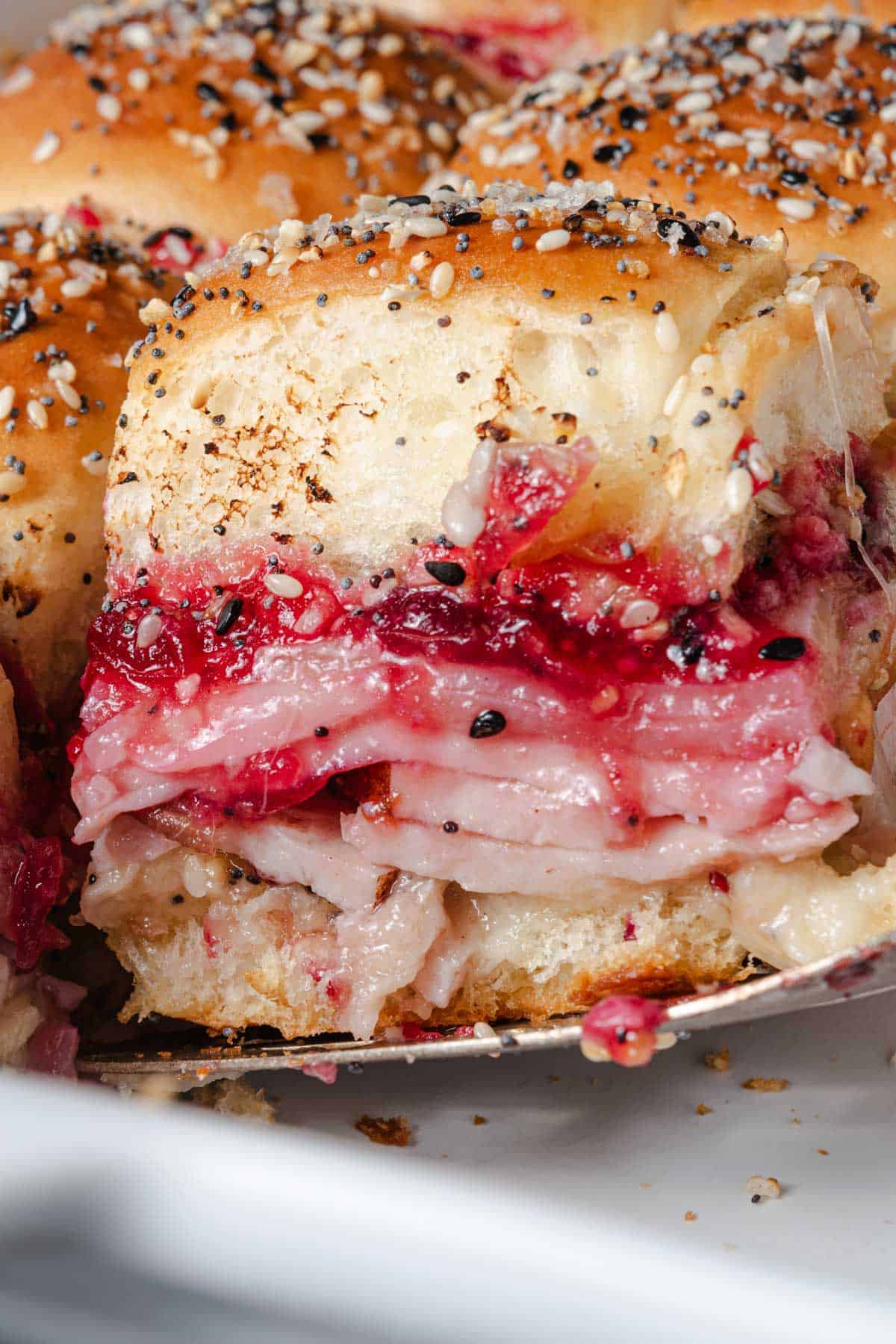 Serving a cranberry sauce, turkey, and cheese slider from a pan.
