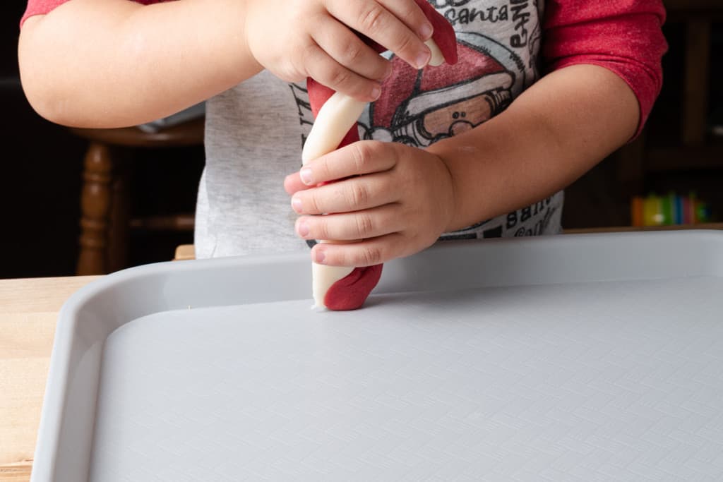 A preschooler shaping a candy cane out of peppermint playdough.