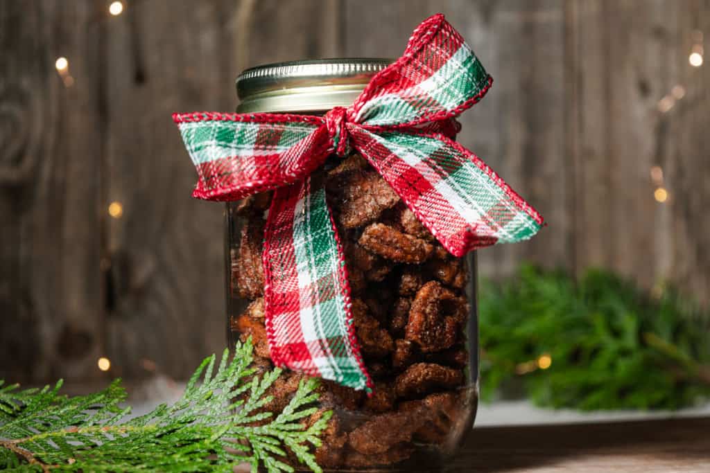 A jar of spicy candied pecans in a jar with a ribbon to give as Christmas gift or thank you idea.