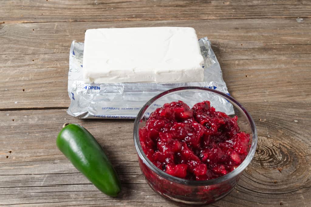 A bowl of cranberry sauce with a whole jalapeno pepper and a block of cream cheese.