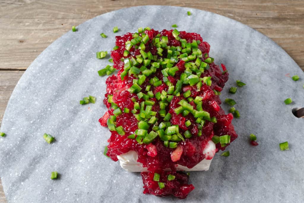 Cranberry sauce and diced jalapeno peppers on a block of cream cheese.